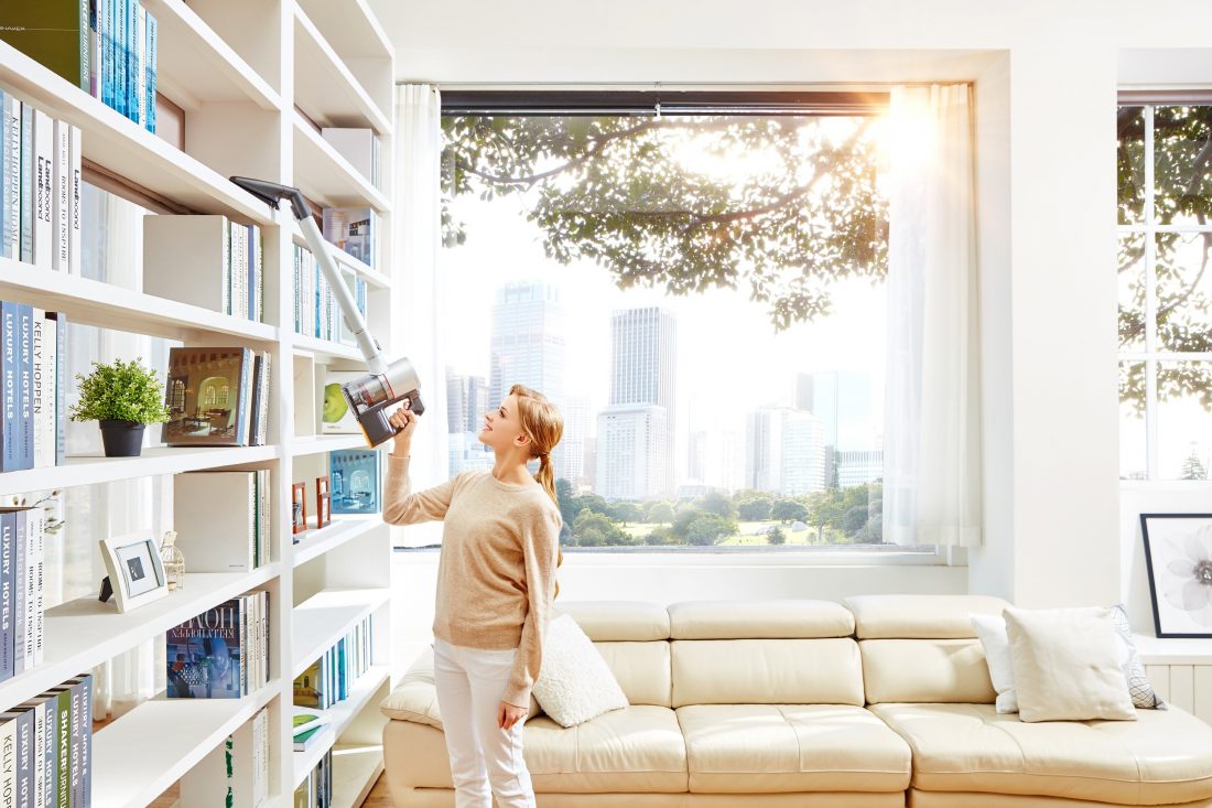 A woman vacuums bookshelves with the LG CordZero Handstick