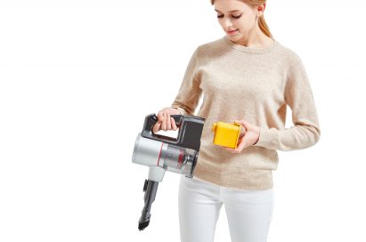 A woman is detaching the battery from the bottom of canister on the LG CordZero Handstick.