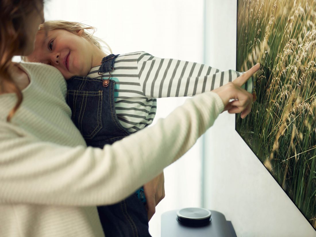 Another view of a mother and small child look at an LG SIGNATURE OLED TV W and the child is touching the screen