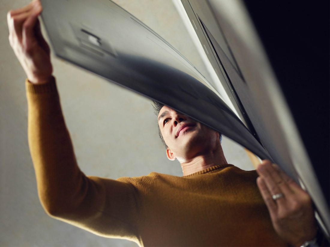 A man tugs on the bottom of the screen of LG SIGNATURE OLED TV W and admires the slender form of it.