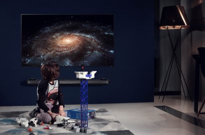 A small boy plays with space toys while the LG SIGNATURE OLED TV W is displayed on the wall with a picture of a galaxy on the screen.