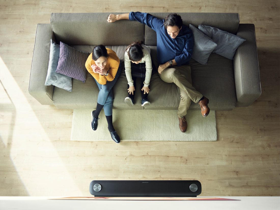Another view of a family sitting in their living room looking at the LG SIGNATURE OLED TV W (model W7) which is mounted on the wall