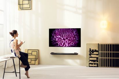 A woman rests against the table looking at an LG SIGNATURE OLED TV W (model W7) mounted on the wall.