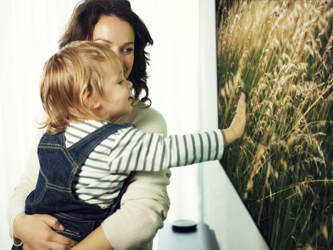 A mother and small child look at an LG SIGNATURE OLED TV W while the child is touching the screen.