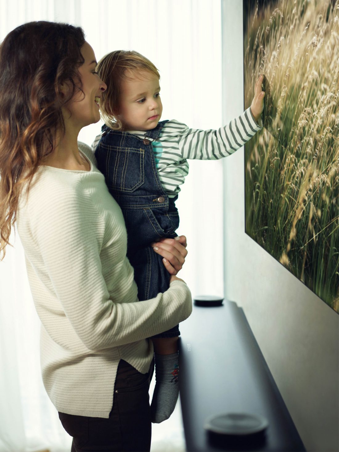 Another view of a mother and small child look at an LG SIGNATURE OLED TV W and the child is touching the screen