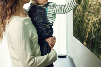 Another view of a mother and small child look at an LG SIGNATURE OLED TV W and the child is touching the screen