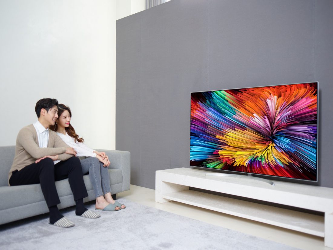 A couple sits on a couch watching the LG SUPER UHD TV (model SJ95).