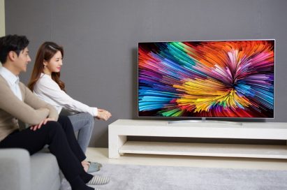 A side view of a couple sitting on a couch while watching colorful imagery on the LG SUPER UHD TV
