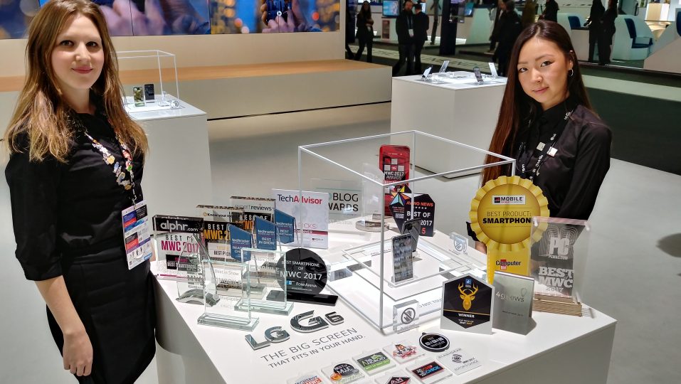 Two LG promoters standing behind two LG G6 devices and 31 booth awards that were given to the LG G6 at MWC 2017