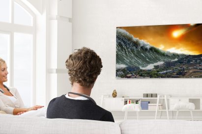 A man and woman are watching television with the LG Tone Studio around both of their necks