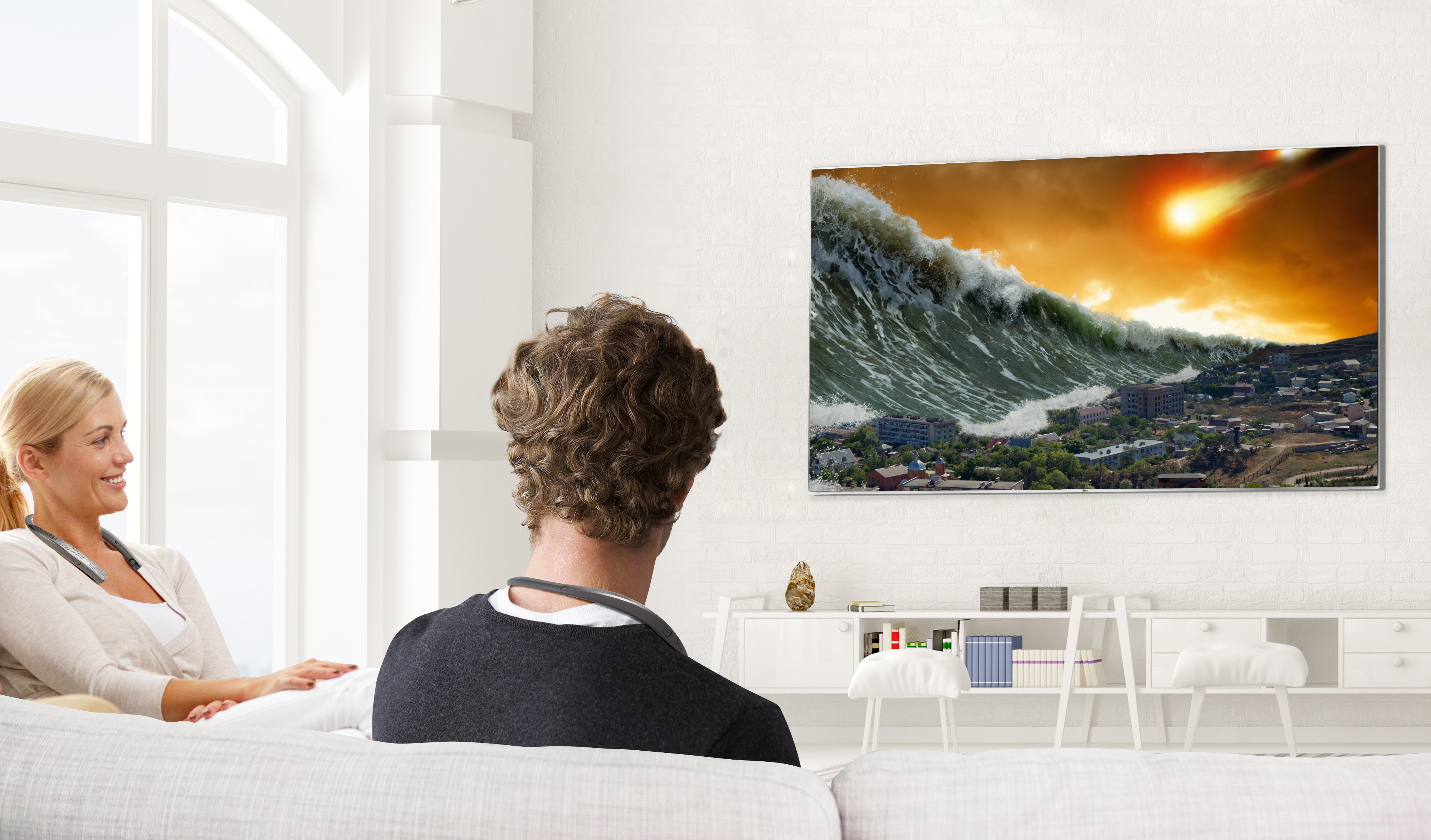 A man and woman are watching television with the LG Tone Studio around both of their necks