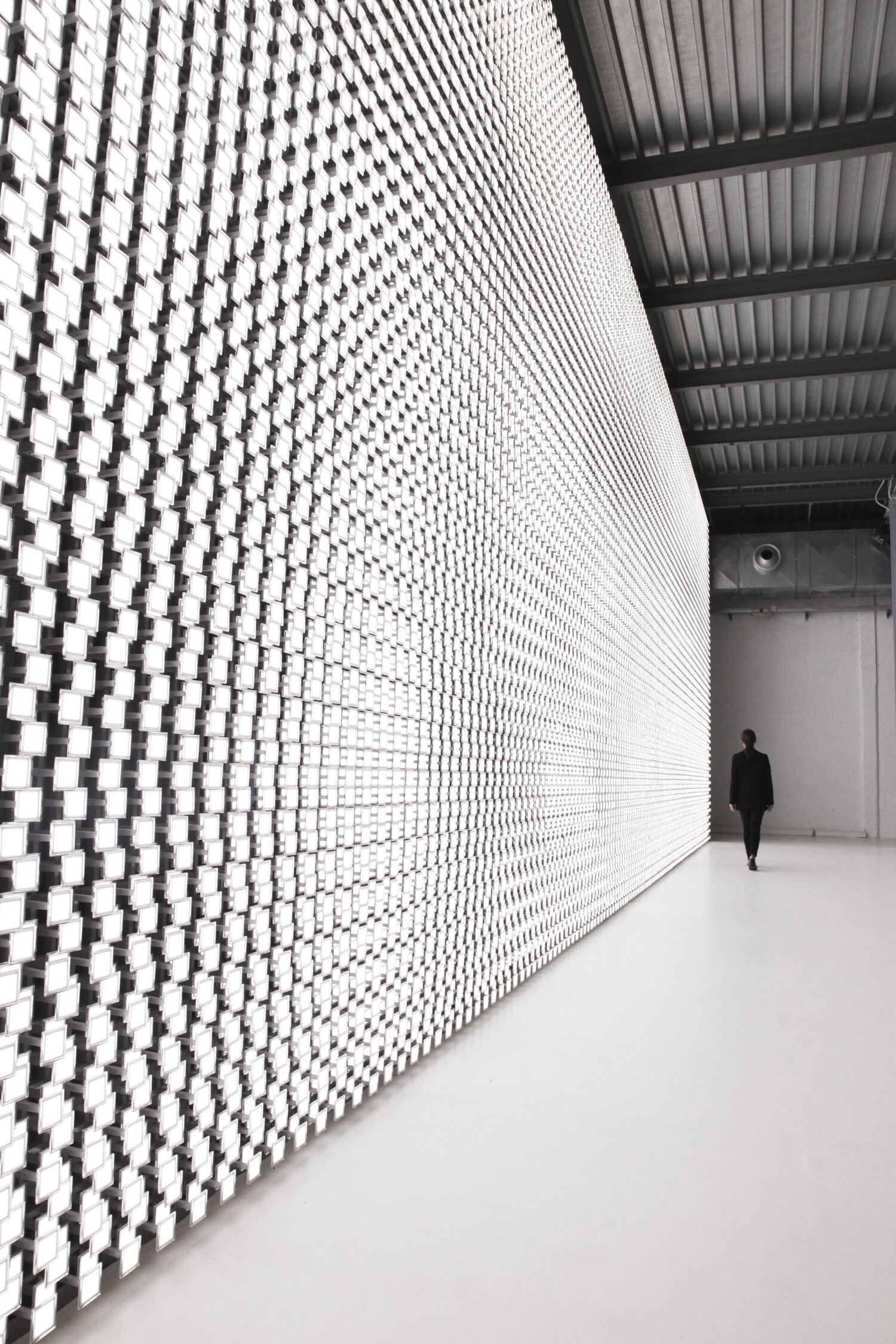 A woman is seen in the background walking beside the back wall of Tokujin Yoshioka’s art exhibition, which boasts thousands of bright lights.