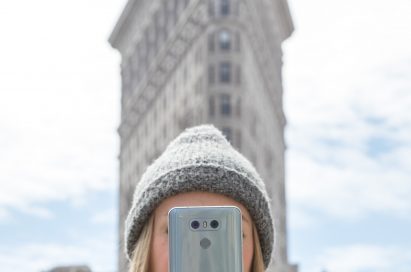 A woman holds the LG G6 in Ice Platinum up in front of her face while standing in front of the Flatiron Building in New York, USA