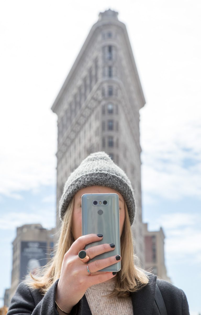 A woman holds the LG G6 in Ice Platinum up in front of her face while standing in front of the Flatiron Building in New York, USA