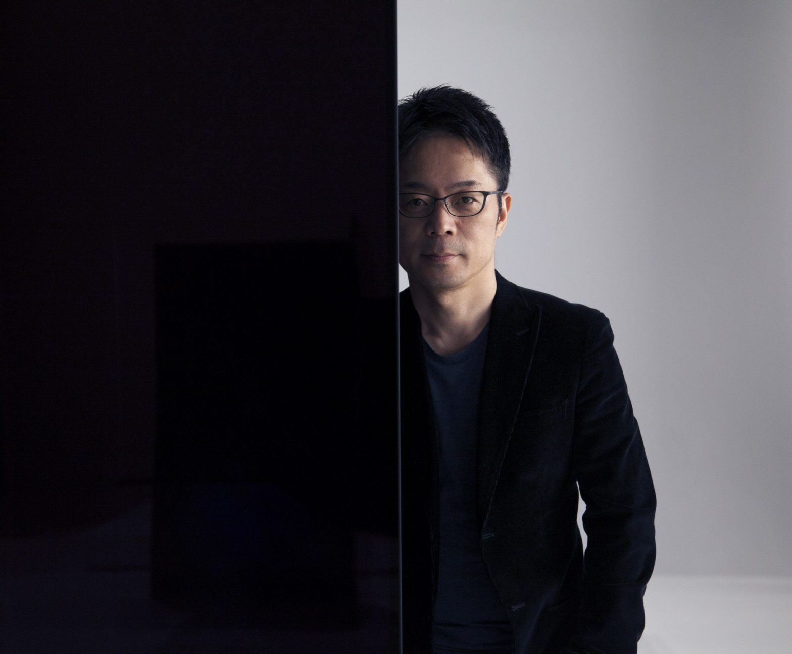 Tokujin Yoshioka stands behind one of LG screens making up his art installation wall looking into the camera.