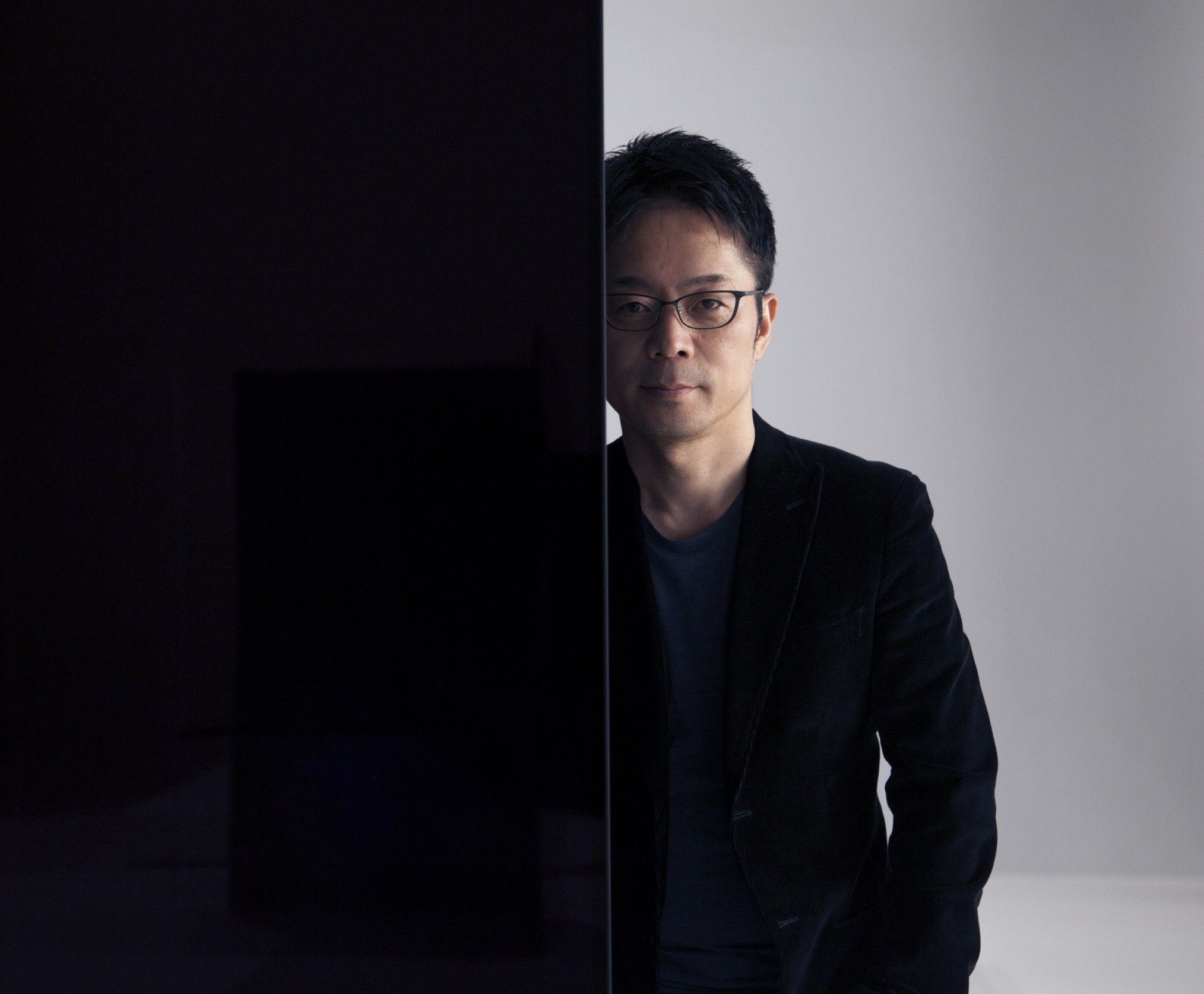 Tokujin Yoshioka stands behind one of LG screens making up his art installation wall looking into the camera.