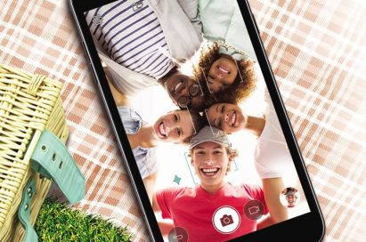 The LG Xpower2 lying on top of a picnic blanket, with a group of people captured in the camera frame while taking a selfie