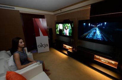 A female model watches Okja on LG’s 2017 SIGNATURE OLED TV W, Netflix promotional standing banner visible at side of room