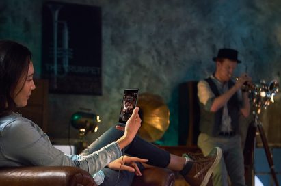 A woman sitting in a chair listening to music with the LG Q8 via headphones