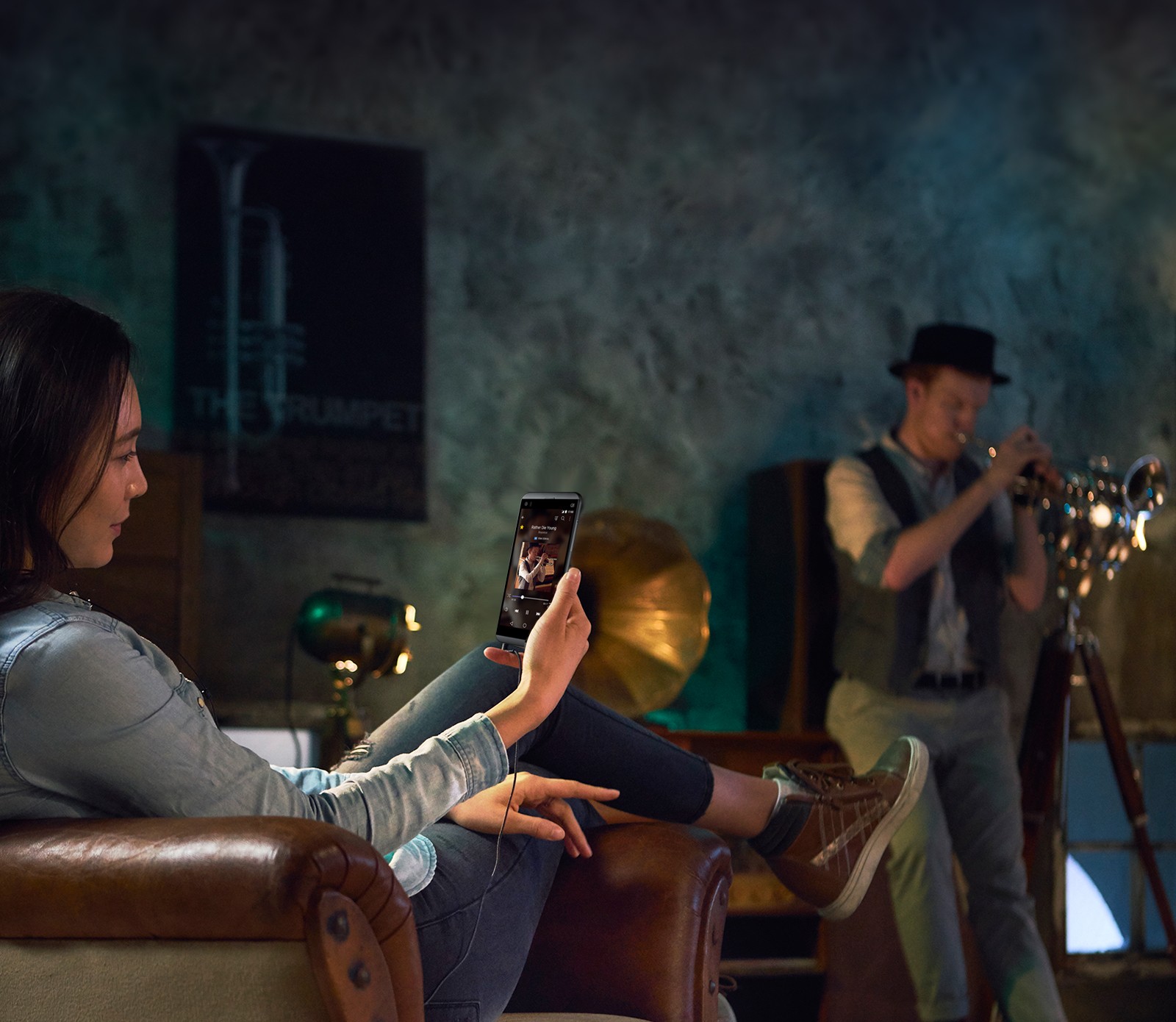 A woman sitting in a chair listening to music with the LG Q8 via headphones