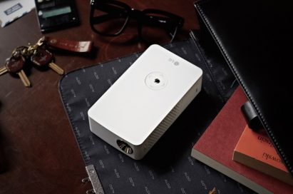 LG MiniBeam Projector model PH30J with scattered objects including a calculator, pair of glasses and keys