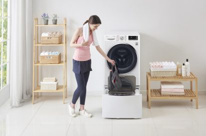 A woman in athletic wear putting gym shorts in the LG TWINWash™ Mini unit of the TWINWash™ washing machine in a laundry room