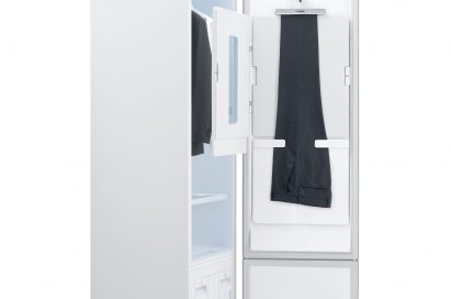 Side view of LG Styler with the door open, showing trousers hanging on the door and a jacket and white shirt hanging inside