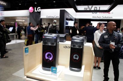 Staff stand next to a display of two LG LOUDR speakers, with several CES attendees looking at LG ThinQ AI kitchen solutions in the background