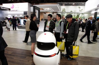 A woman explains and demonstrates the LG CLOi GuideBot to three CES 2018 visitors at the LG booth