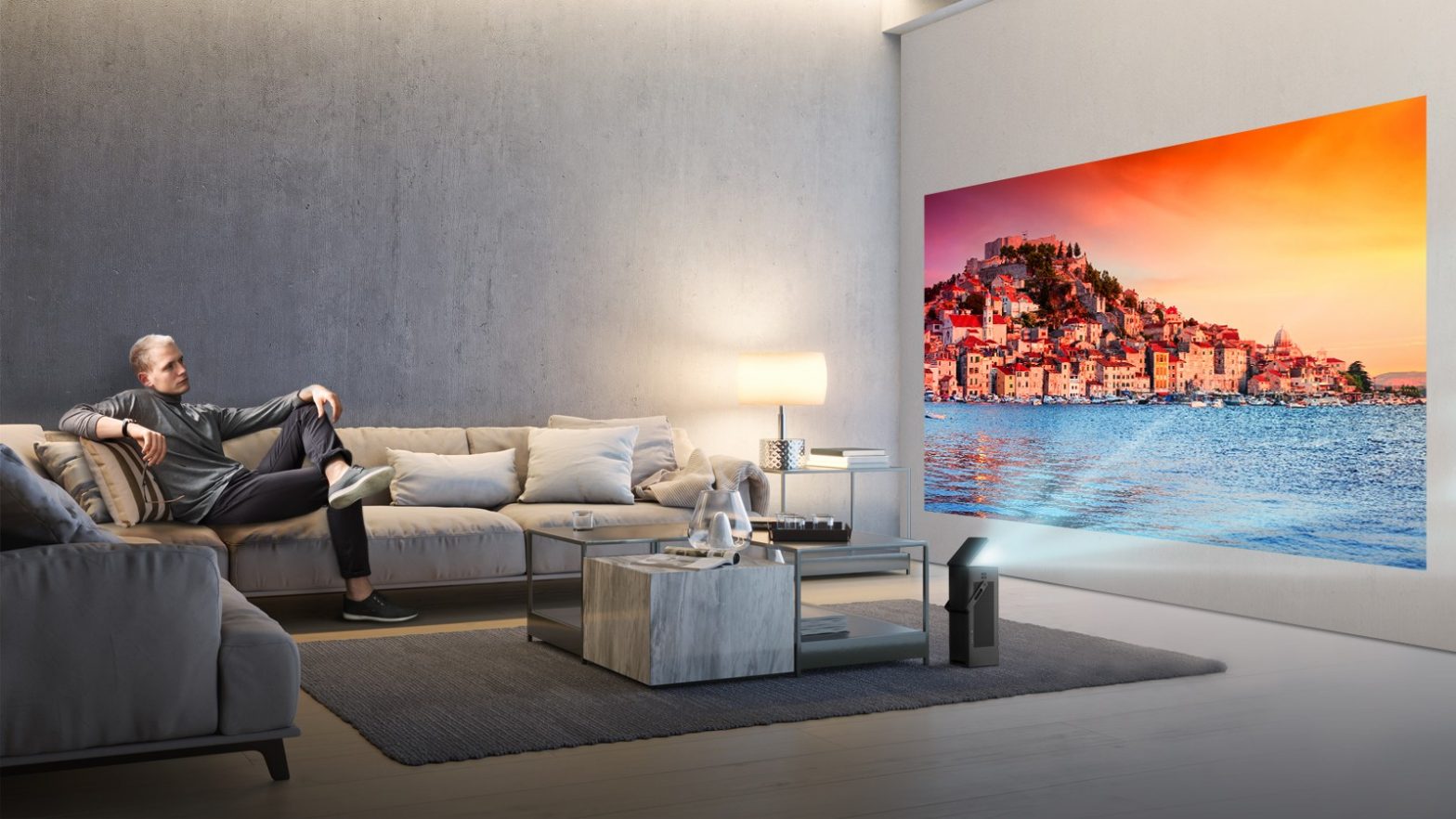 A man seated on a couch watches video projected onto a wall from LG’s HU80K series 4K UHD projector