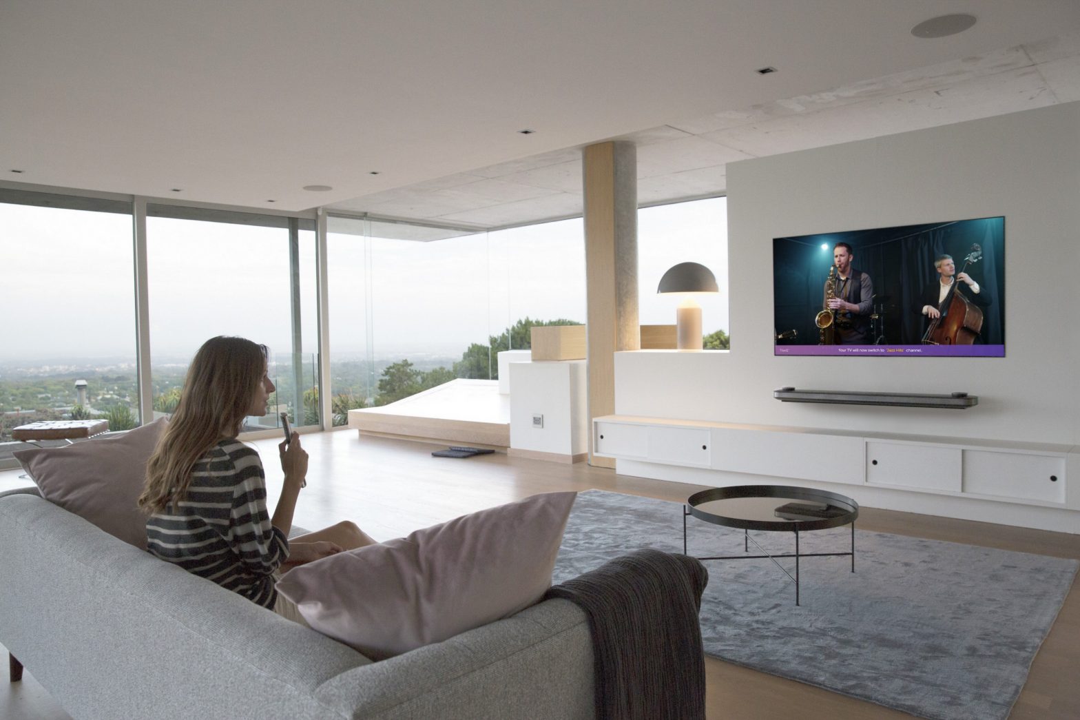 A woman sitting on a couch in a modern apartment watching a jazz band play on her LG AI OLED TV