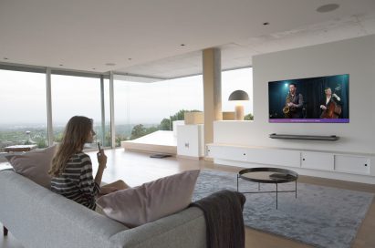 A woman sitting on a couch in a modern apartment watching a jazz band play on her LG AI OLED TV
