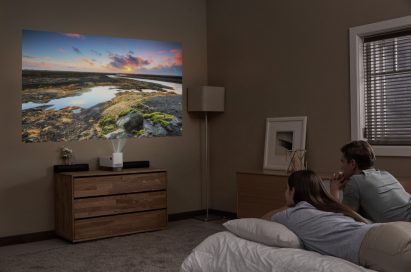 A couple lying in bed while watching a movie projected on the wall by the LG ProBeam Projector HF85J