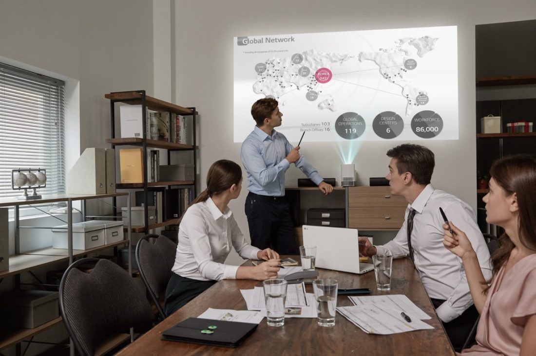 People in a business meeting watch a presentation that is being projected on the wall by the LG ProBeam Projector HF85J.