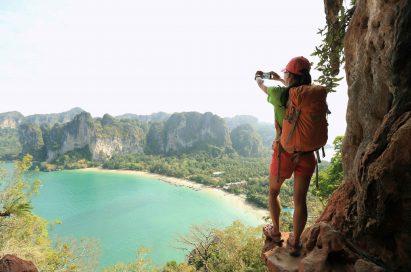 A woman stands in a nature scene taking a photo of the view with the LG X Venture.