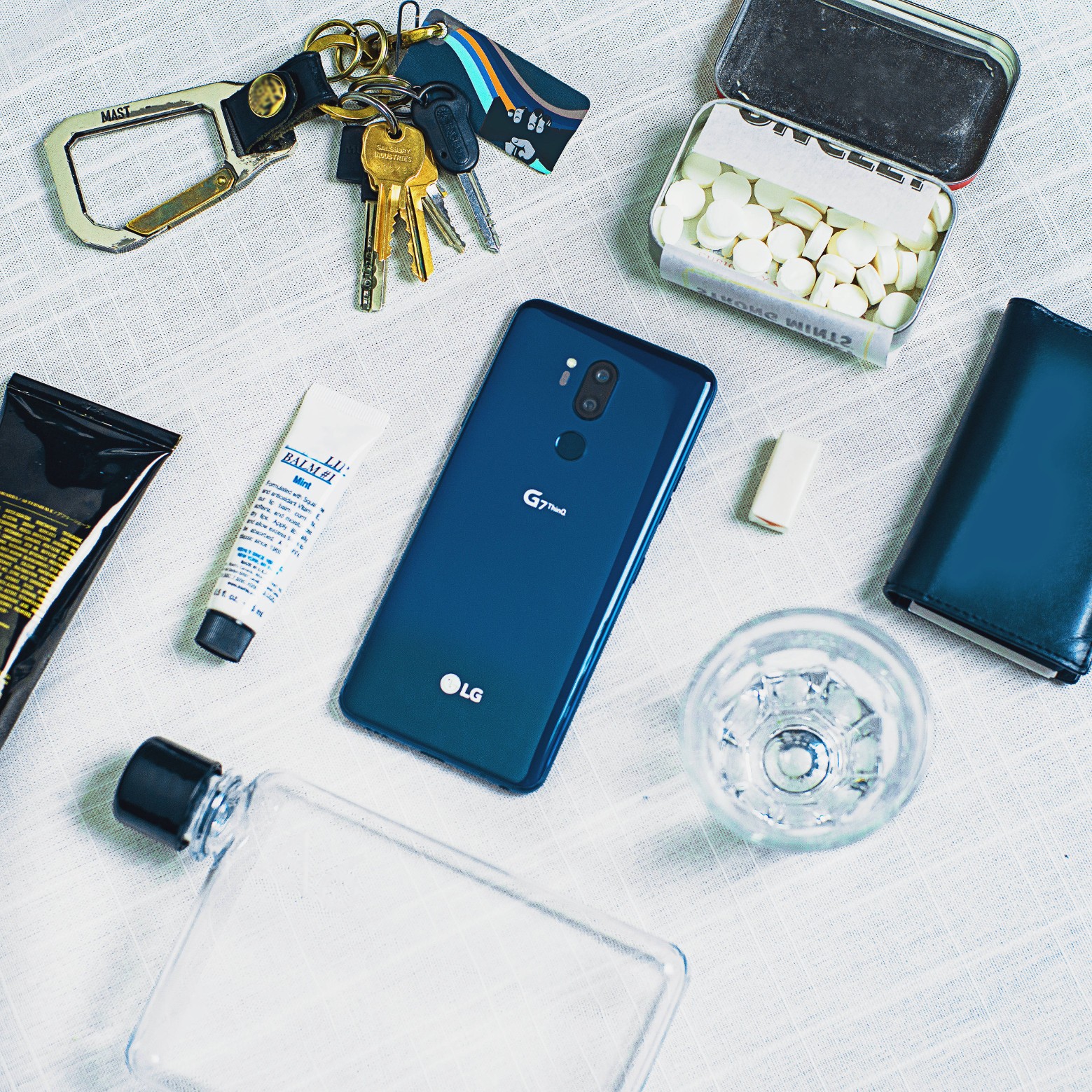 The LG G7 ThinQ in New Moroccan Blue face down on a table, next to other lifestyle items, such as keys, a water bottle, mints, etc.