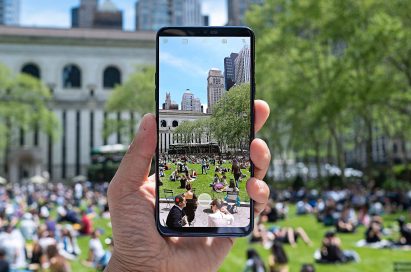 A person holding the LG G7 ThinQ and taking a picture of crowded park in the city