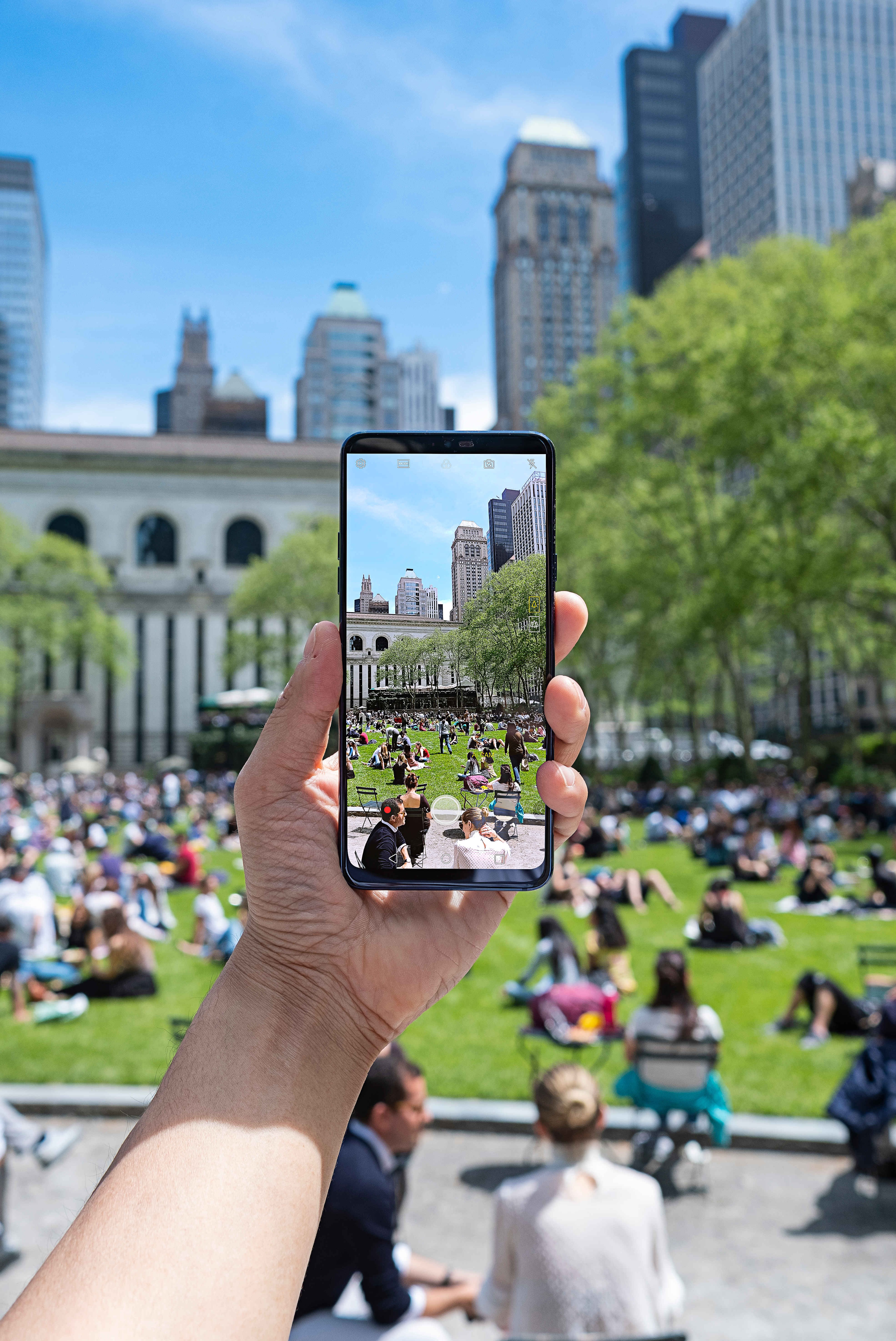 A person holding the LG G7 ThinQ and taking a picture of crowded park in the city