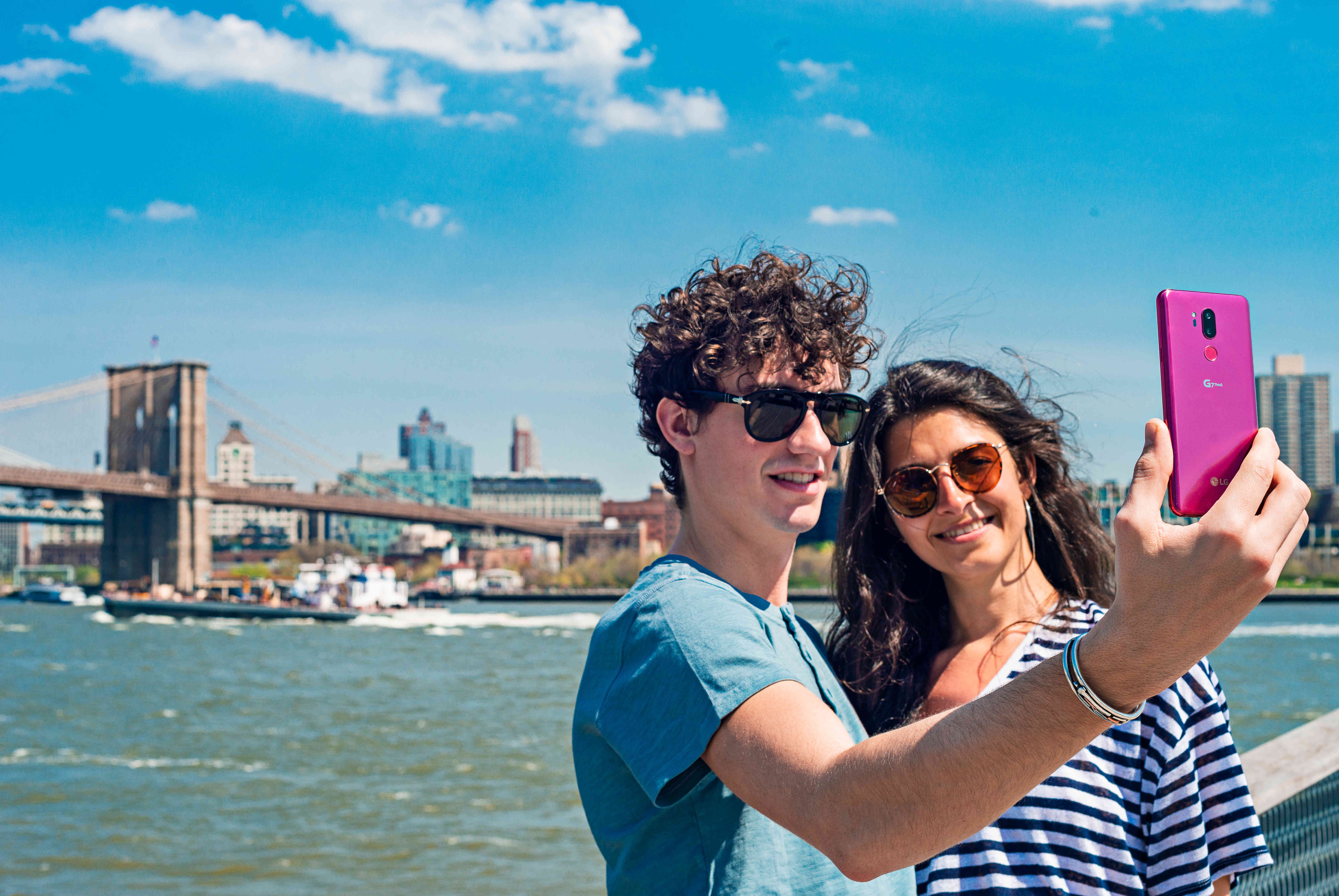 A man and woman taking a selfie in front of a riverfront with the LG G7 ThinQ in Raspberry Rose
