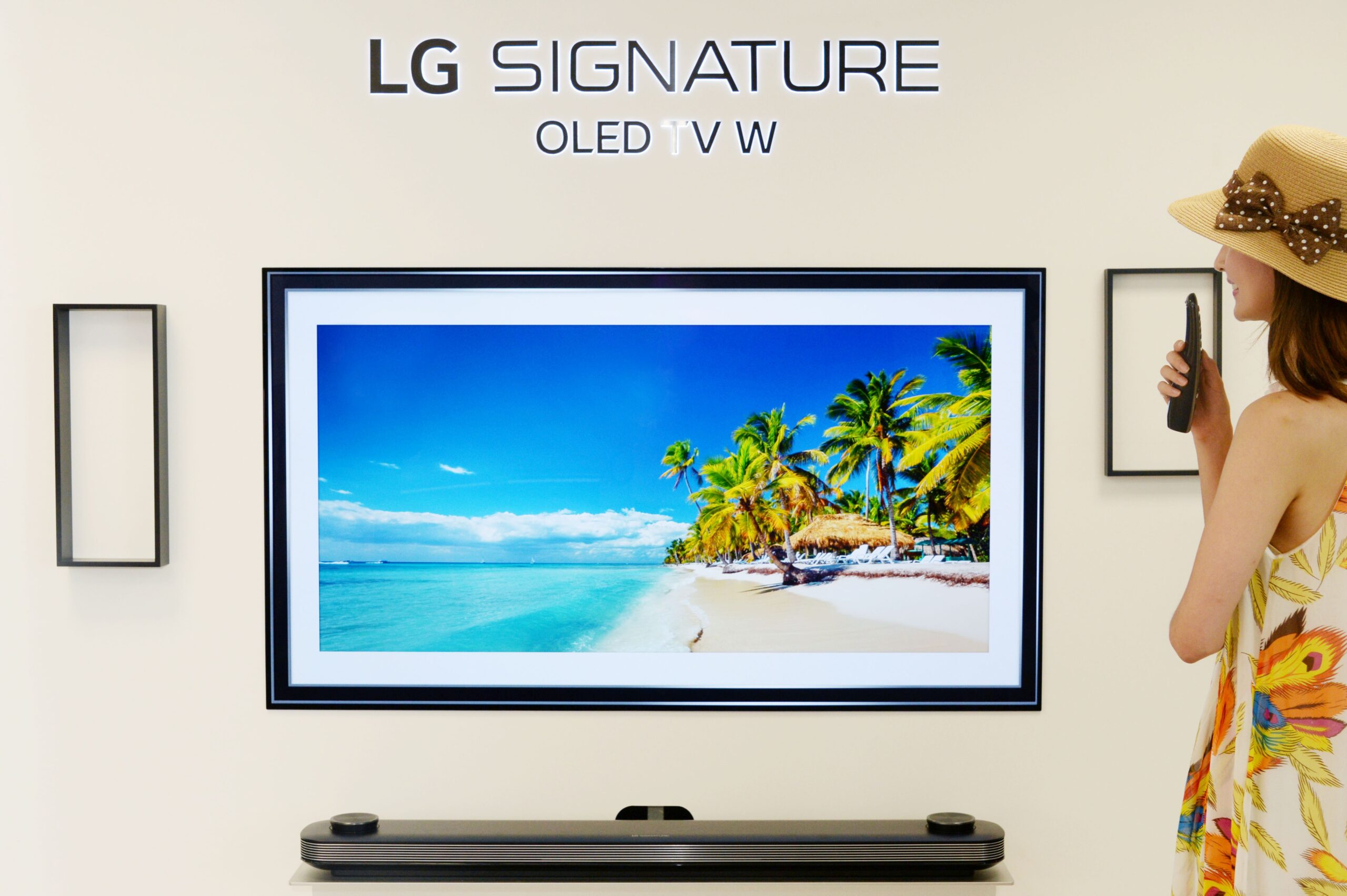 A woman looks at LG SIGNATURE OLED TV W which displays the tropical beach and coconut trees on its screen.