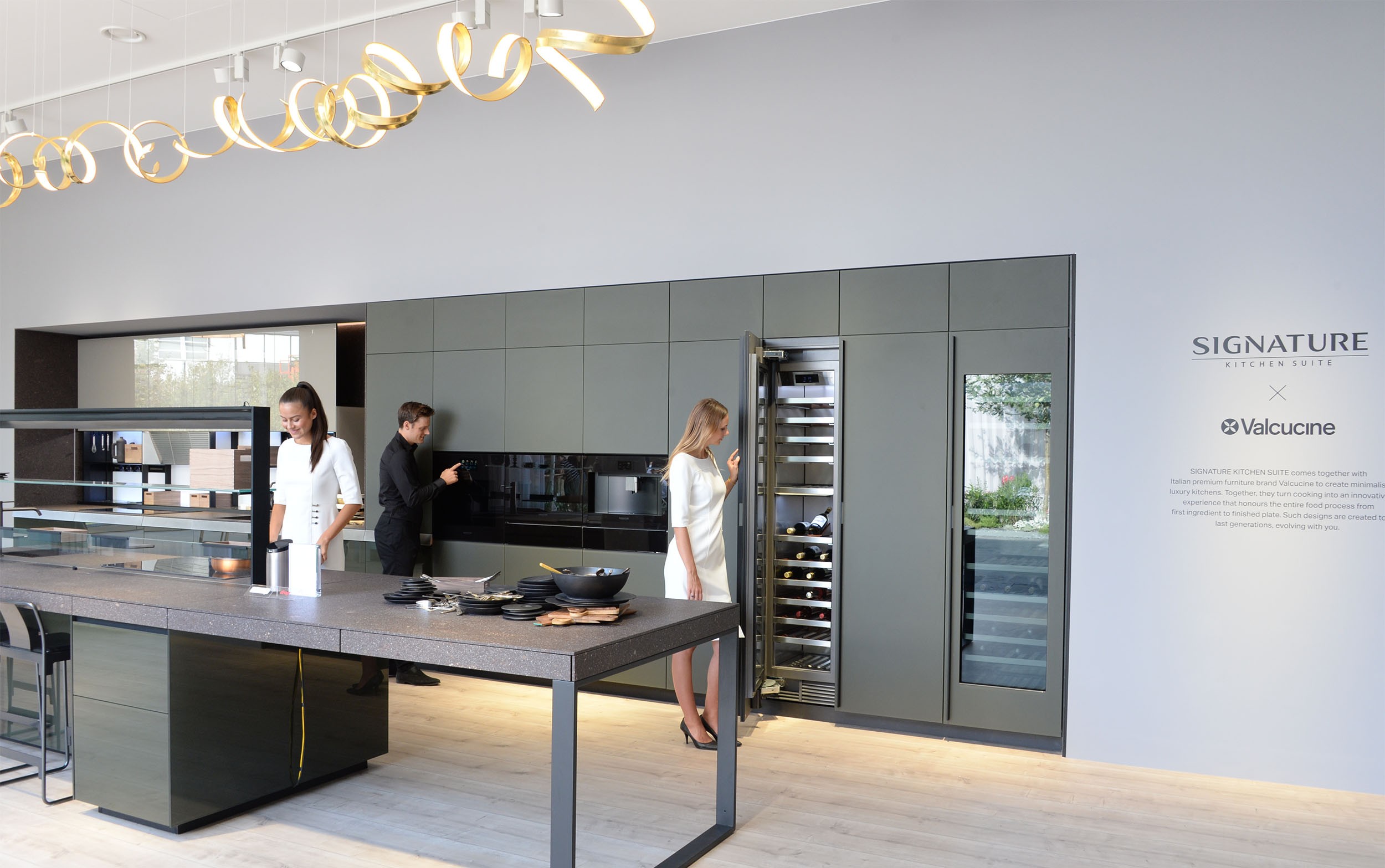 Woman trying cooktop, man trying wall oven and woman opening wine cellar at SIGNATURE KITCHEN SUITE’s exhibition hall cooperated with Valcucine at IFA 2018