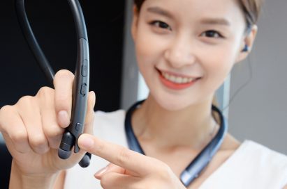 A woman with the LG TONE Platinum SE in Black around her neck pointing at the Google Assistant button on the LG TONE Platinum SE in her hands