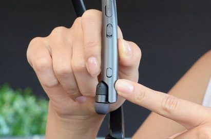 A woman pointing at the Google Assistant button on the LG TONE Platinum SE in her hands