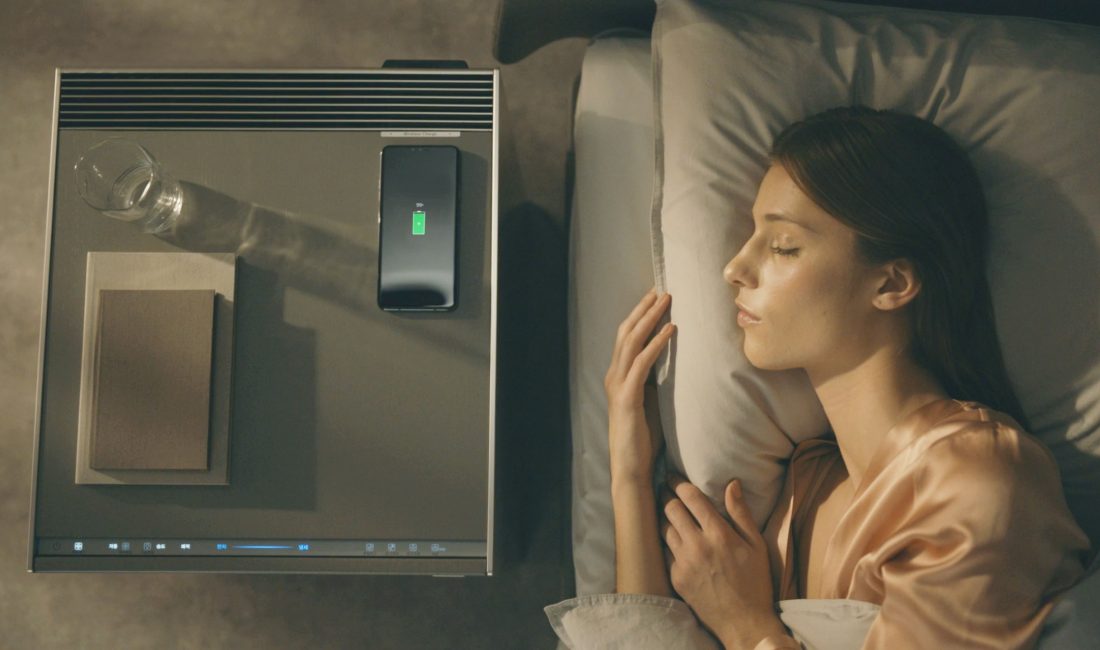 A woman sleeps with an LG OBJET Air Purifier next to her bed; a glass of water, smartphone and books have been placed on top of the purifier