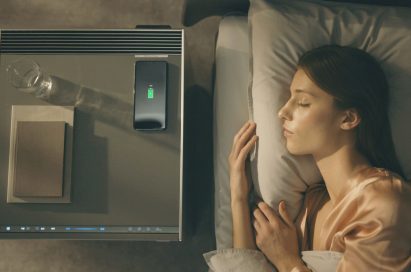 A woman sleeps with an LG OBJET Air Purifier next to her bed; a glass of water, smartphone and books have been placed on top of the purifier