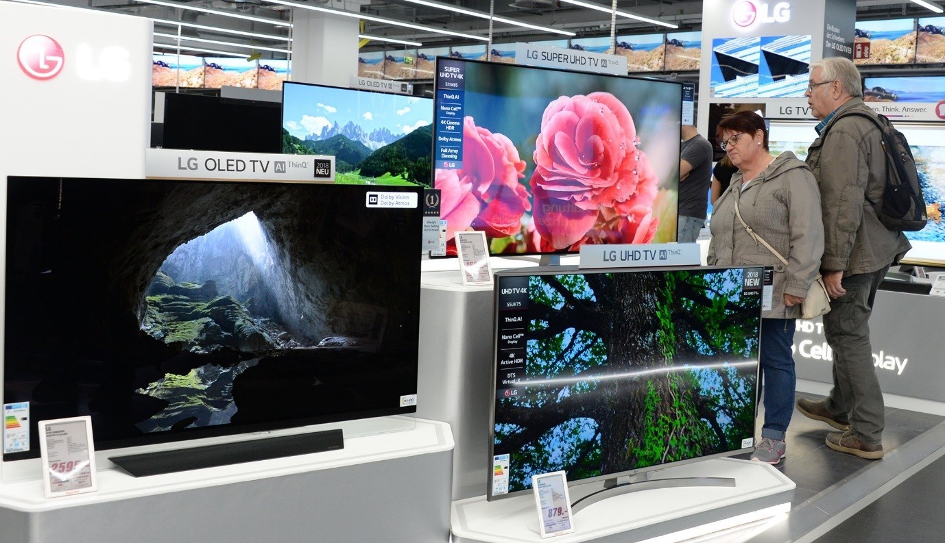 A consumer examines the highly thin depth of LG's SUPER UHD TV while some other consumers look around other TV products at LG's store.