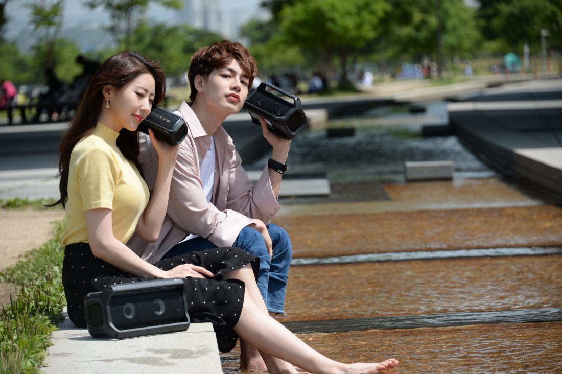 A man and a woman sitting outside enjoying music on their LG XBOOMs