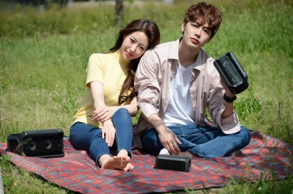 A man and a woman sitting outside on a picnic blanket enjoying music on their LG XBOOMs
