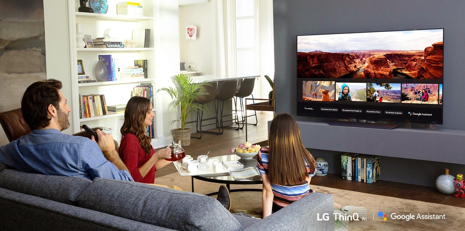 A family sits in the living room while looking at their travel photos via Google Assistant on LG’s ThinQ TV.