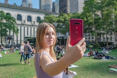 A woman holds up and looks at the display of the LG V40 ThinQ in the Carmine Red color.